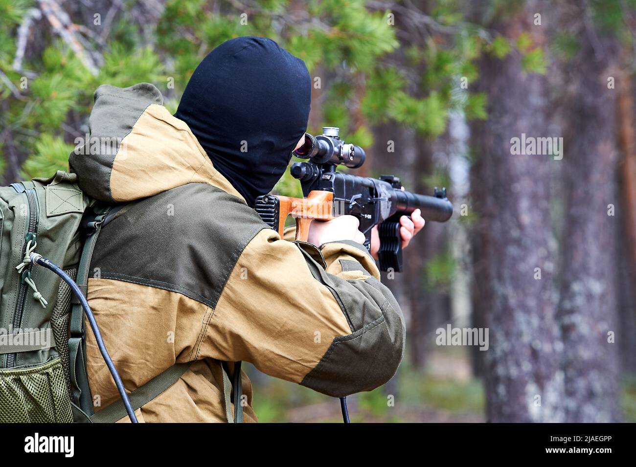Un uomo in balaclava con un fucile da cecchino che mira nei boschi Foto Stock