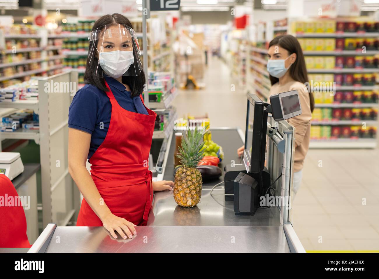 Cassa supermercato e cliente seguendo le norme di protezione personale durante le giornate di quarantena del coronavirus, indossare maschere Foto Stock