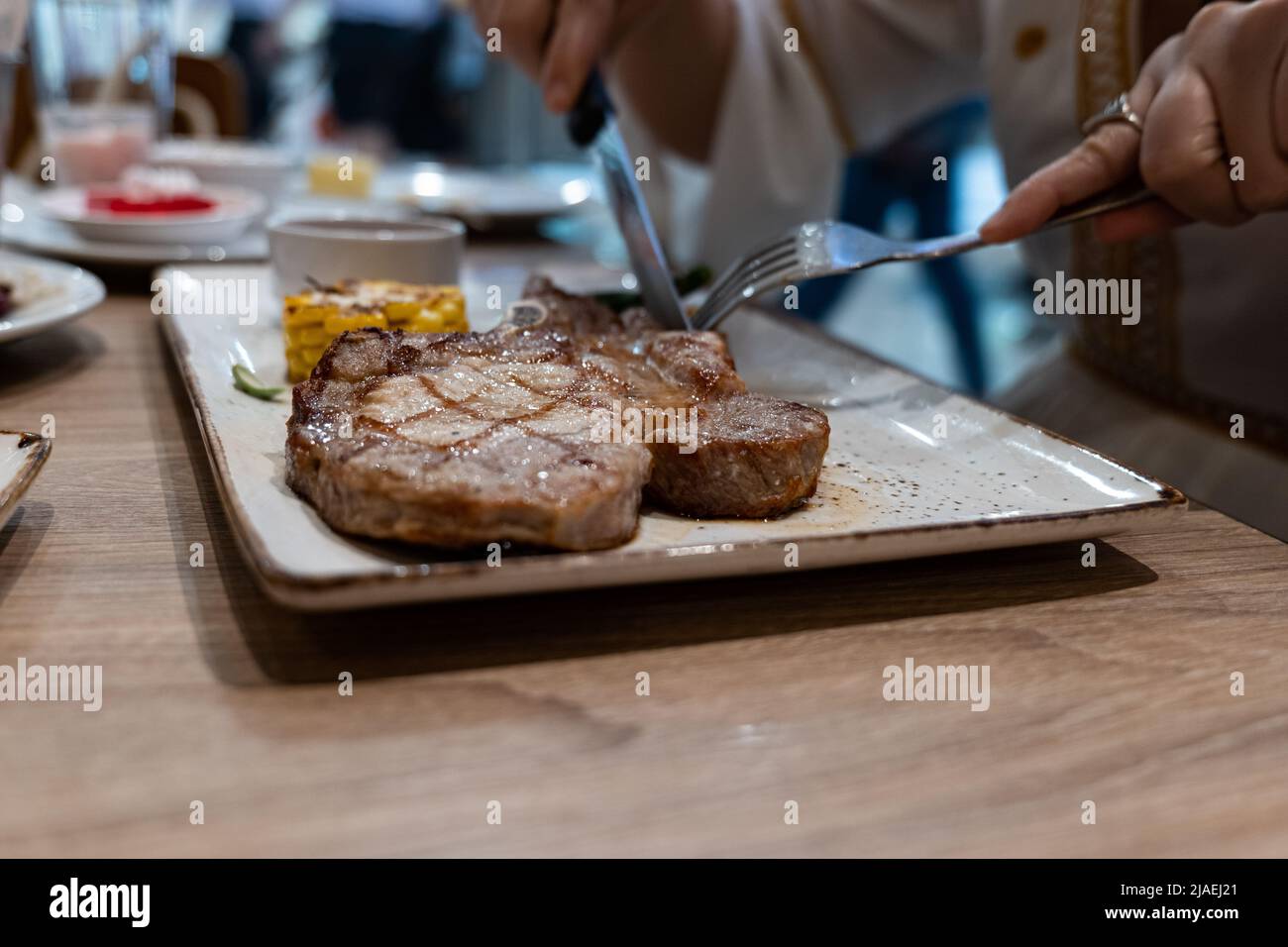 Primo piano vista parziale della donna Godetevi mangiare bistecca con forchetta e coltello nel ristorante Foto Stock