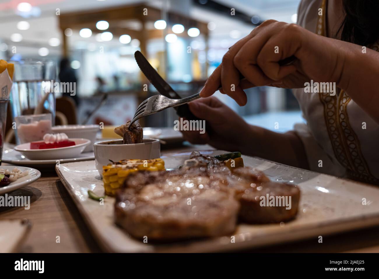 Primo piano vista parziale della donna Godetevi mangiare bistecca con forchetta e coltello nel ristorante Foto Stock