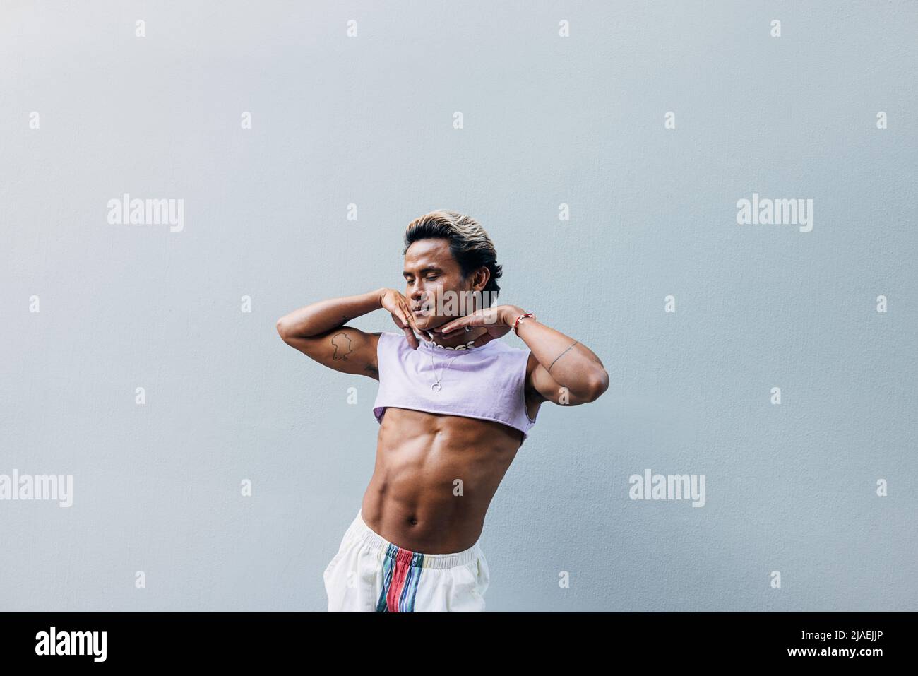 Giovane uomo bello che si posa contro il muro grigio in abiti eleganti Foto Stock