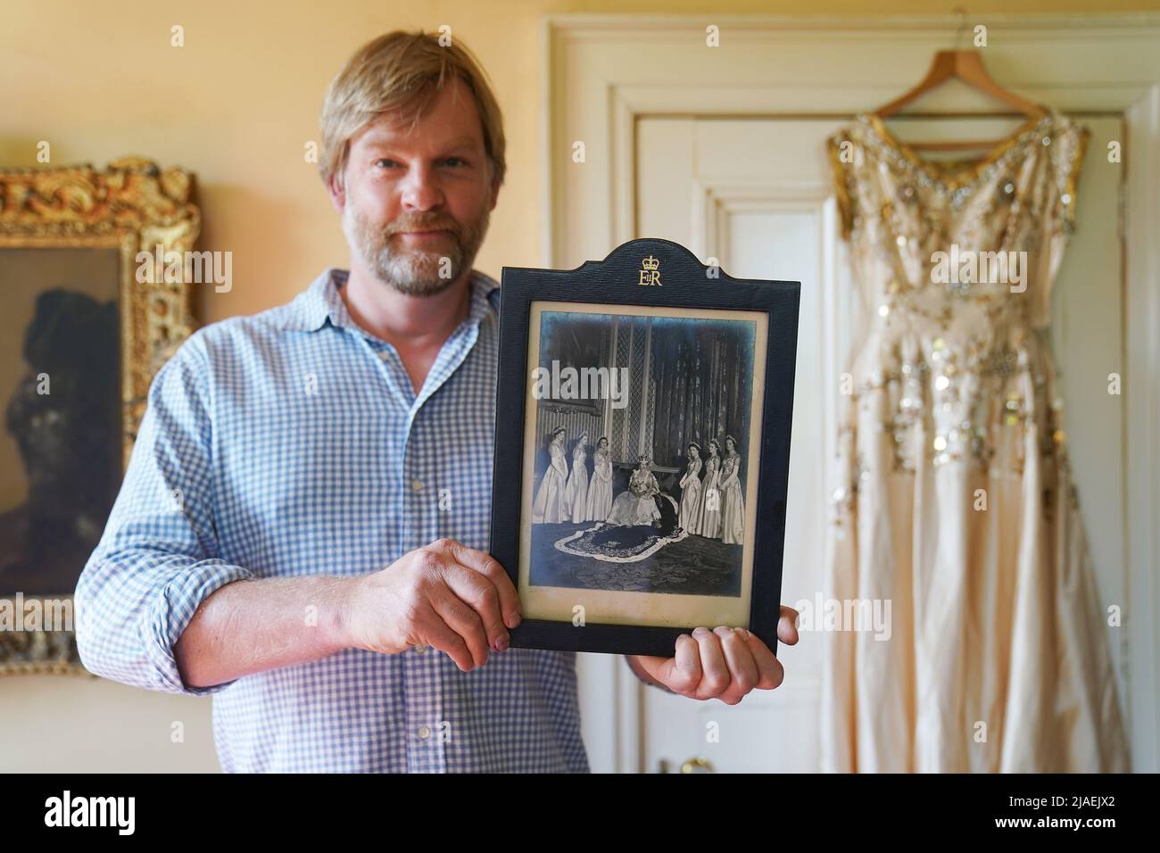 Rory Campbell, nella sua casa a Randalstown, Co. Antrim, tenendo una fotografia di sua madre Lady Moyra Campbell (a sinistra) con la regina Elisabetta II il giorno dell'incoronazione, insieme al vestito Lady Campbell indossava come una cameriera d'onore all'incoronazione della regina nel 1952. L'abito sarà esposto come parte di una speciale mostra giubilare di diamanti al Castello di Enniskillen. Data immagine: Giovedì 26 maggio 2022. Foto Stock