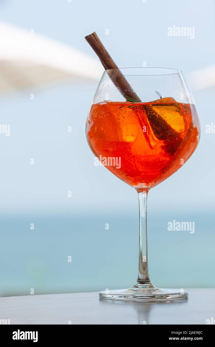 Un bicchiere di cocktail d'arancia mette sul tavolo con ombrello sfocato e sfondo marino per il concetto di bevanda estiva e di vacanza. Foto Stock
