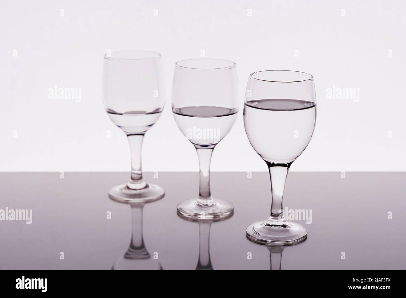 Tre bicchieri di vino riempiti di acqua riflessa sul tavolo Foto Stock