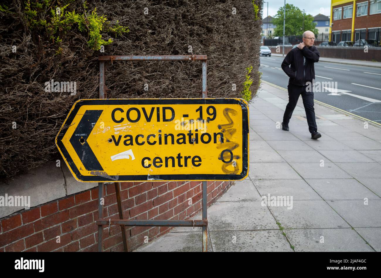 Un uomo cammina oltre un cartello per un centro di vaccinazione COVID-19 a Portsmouth, Hampshire, Inghilterra. Foto Stock