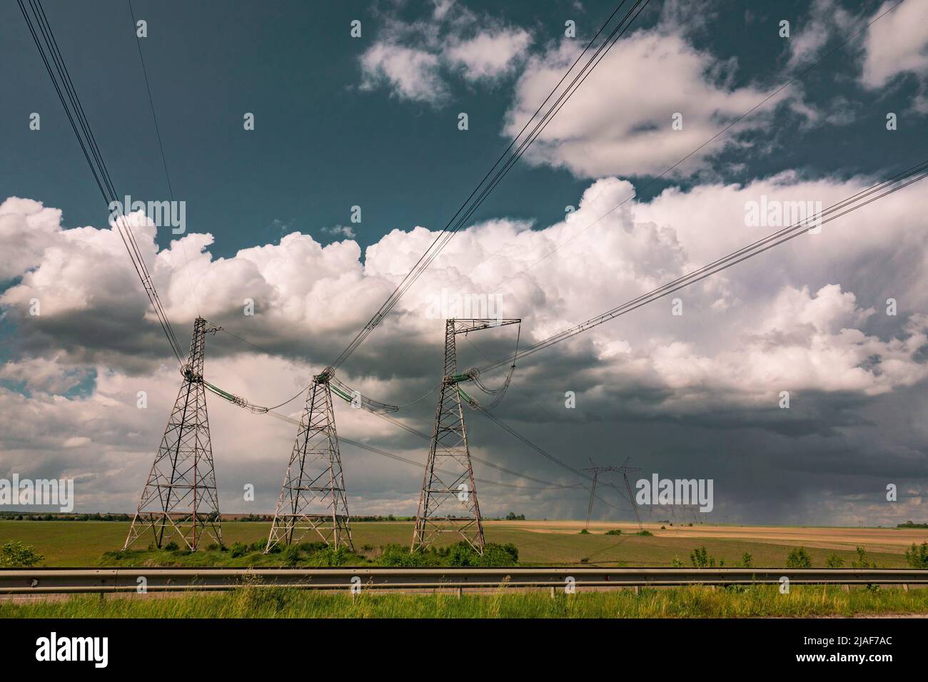 Linee elettriche contro il cielo drammatico. Campo di campagna con piloni di linea di alimentazione. Foto Stock