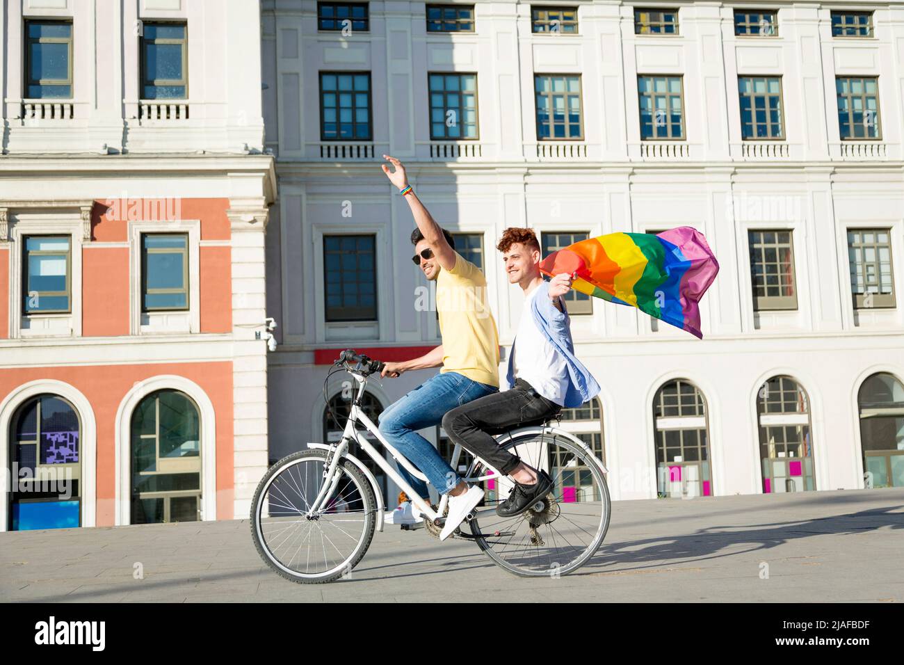 I giovani gay si accoppiano con le biciclette a cavallo con la bandiera gay Pride all'aperto. lgbt Concept Foto Stock
