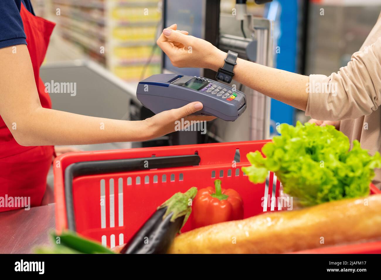 Giovane donna moderna che usa la tecnologia intelligente dell'orologio per pagare merci in moderno supermercato Foto Stock