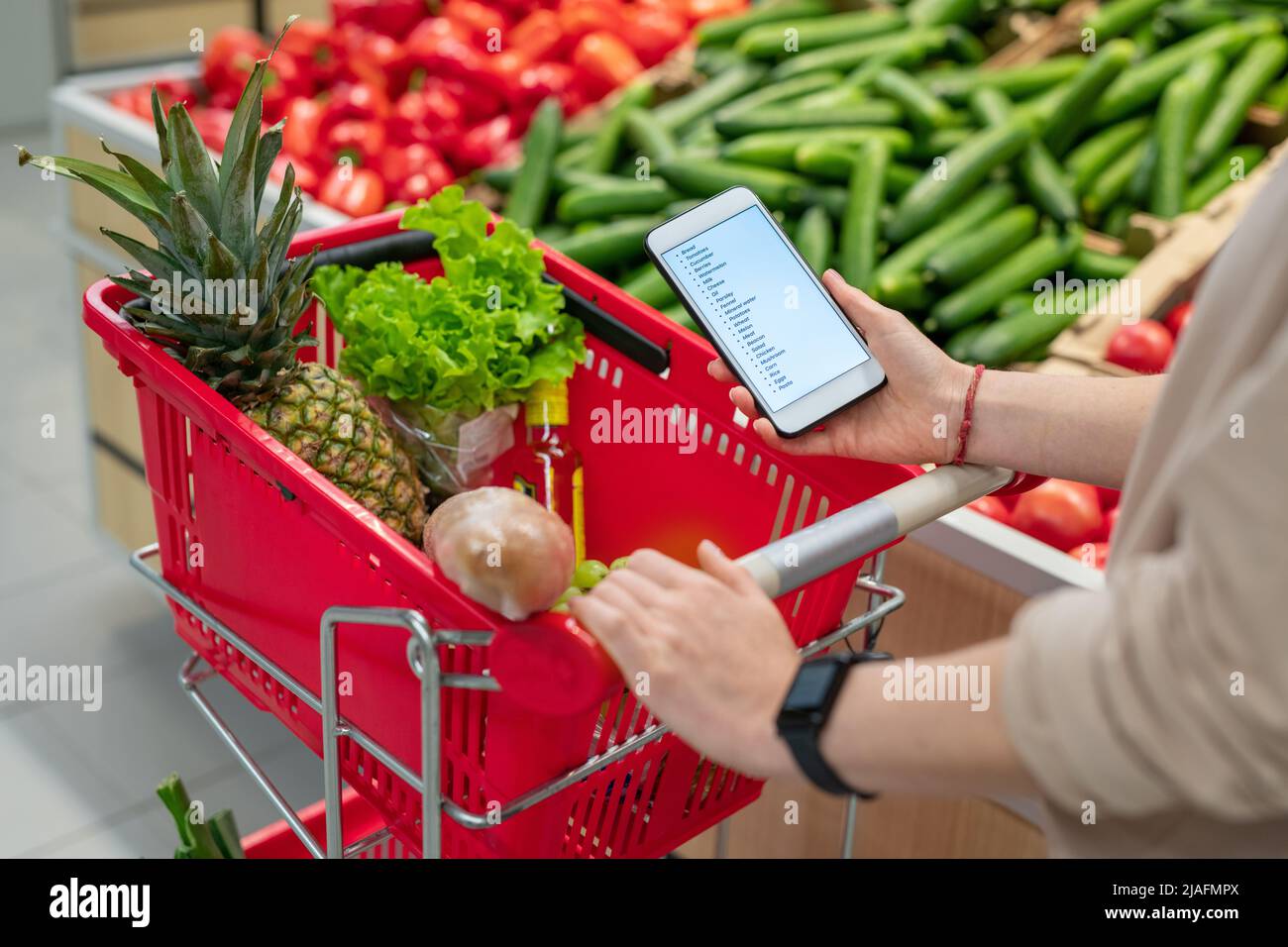 Persona riconoscibile con carrello di shopping nel supermercato guardando lo shopping elenco sullo smartphone Foto Stock