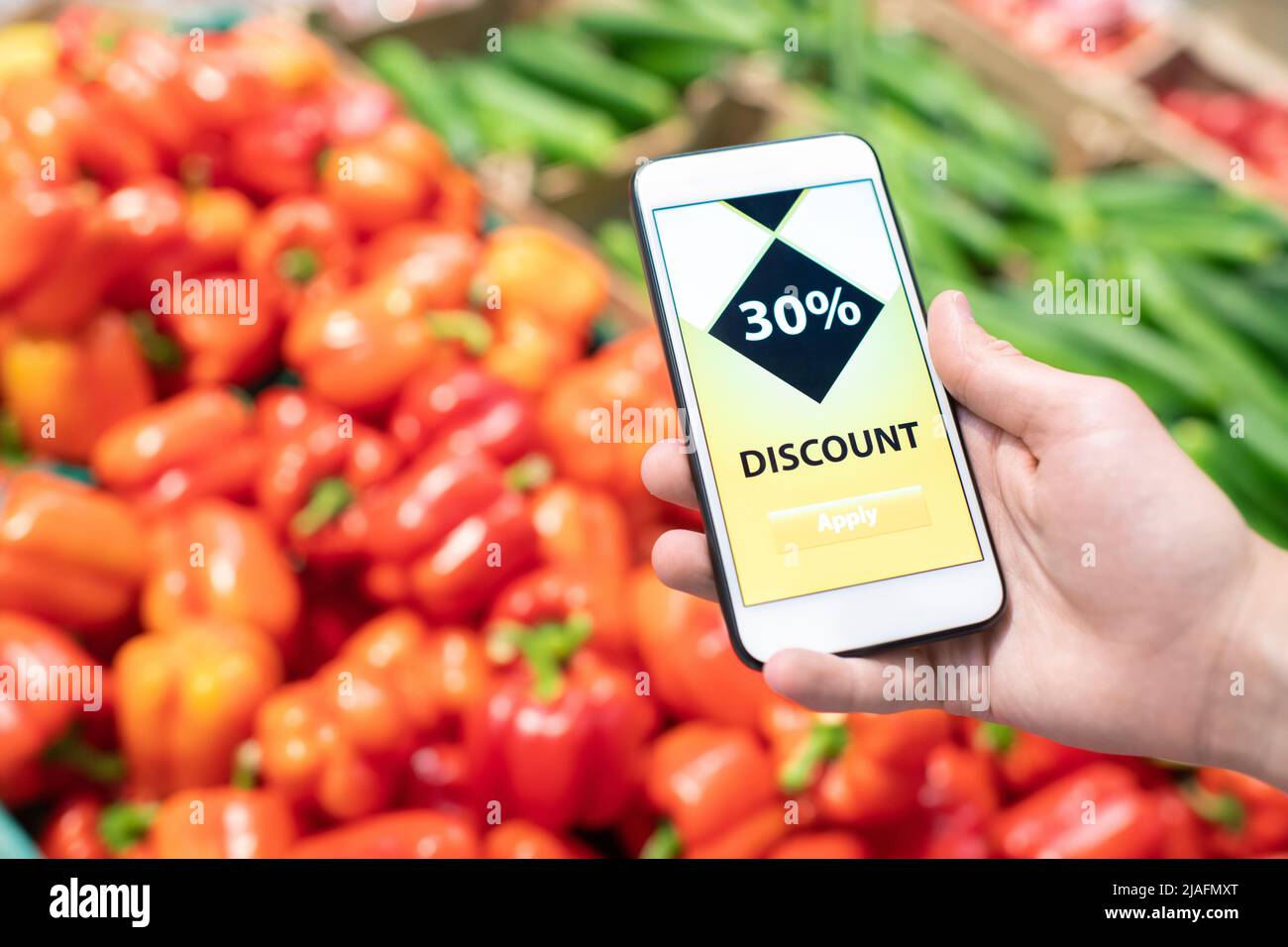 Horizaontal primo piano di uno smartphone irriconoscibile che tiene la mano con sconto applicazione sul suo schermo con frutti sullo sfondo Foto Stock