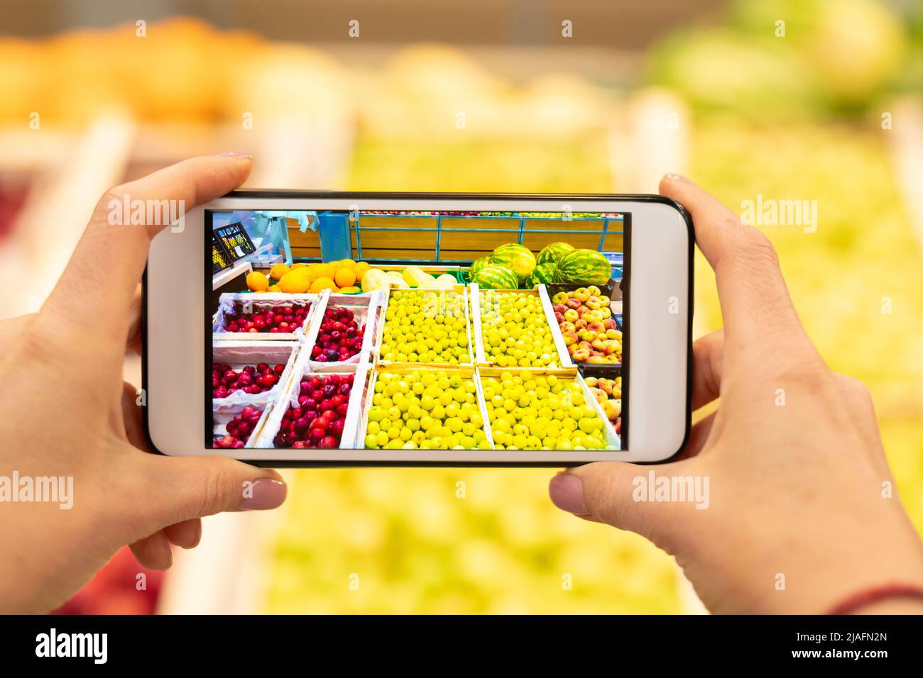 Horizaontal primo piano di uno smartphone irriconoscibile che tiene la mano con sconto applicazione sul suo schermo con frutti sullo sfondo Foto Stock