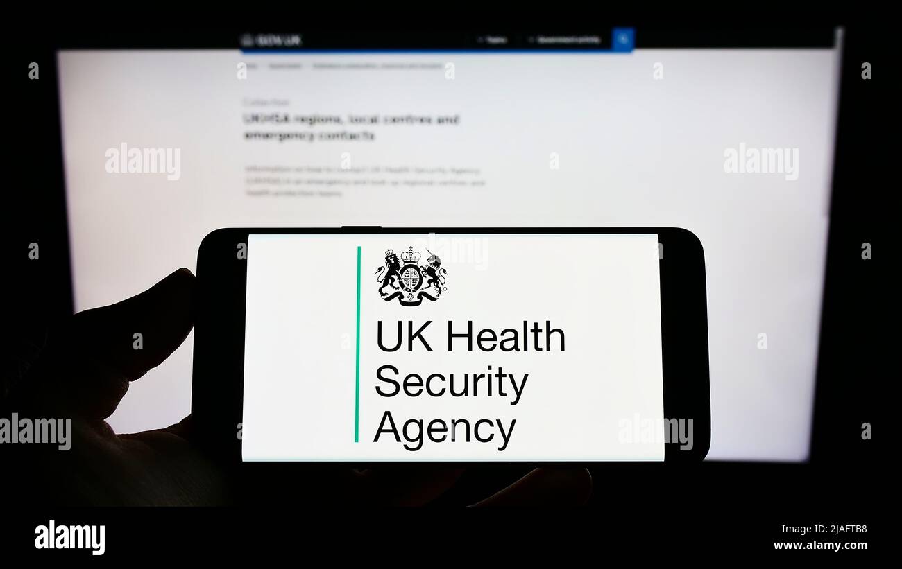 Persona che detiene il cellulare con il logo dell'agenzia UK Health Security Agency (UKHSA) sullo schermo di fronte alla pagina web. Mettere a fuoco sul display del telefono. Foto Stock
