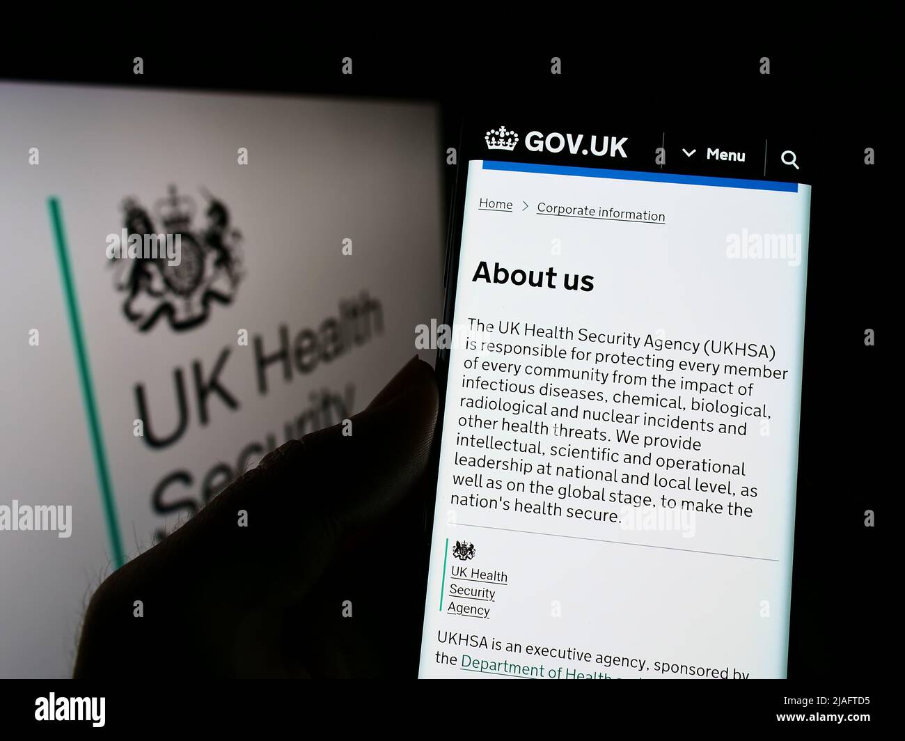 Persona che tiene lo smartphone con la pagina web dell'agenzia UK Health Security Agency (UKHSA) sullo schermo davanti al logo. Concentrarsi sul centro del display del telefono. Foto Stock