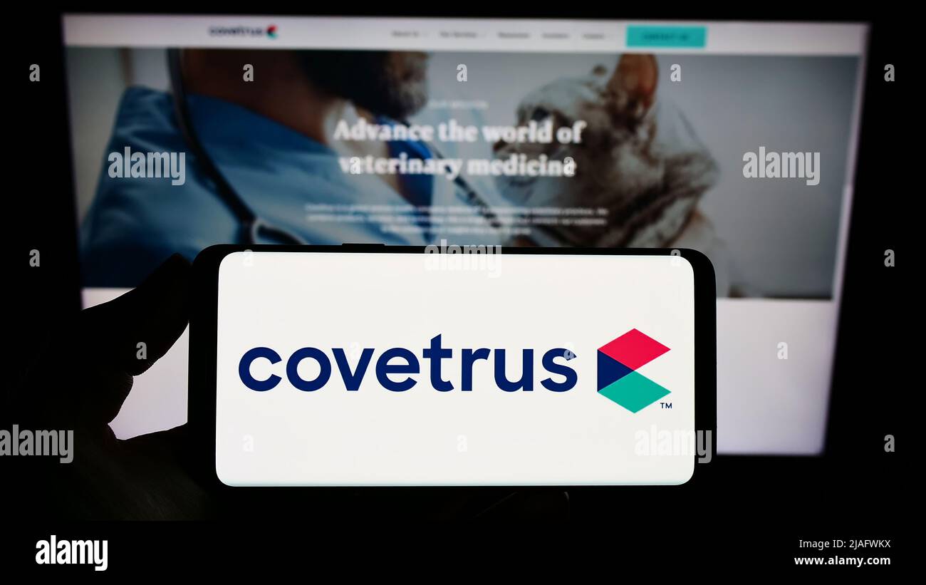 Persona che tiene uno smartphone con il logo della società statunitense per la salute degli animali Covetrus Inc. Sullo schermo di fronte al sito Web. Mettere a fuoco sul display del telefono. Foto Stock