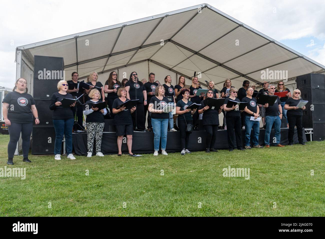 VoxChoir, un gruppo di canto sociale, che si esibisce sul palco in un evento all'aperto a Farnborough, Hampshire, Inghilterra, Regno Unito Foto Stock