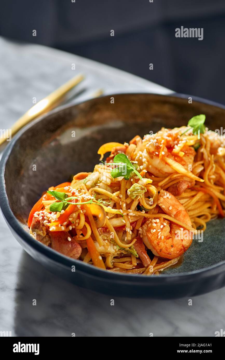 Mescolare le tagliatelle con verdure, gamberetti e frutti di mare in una ciotola nera su un tavolo di marmo. Foto Stock