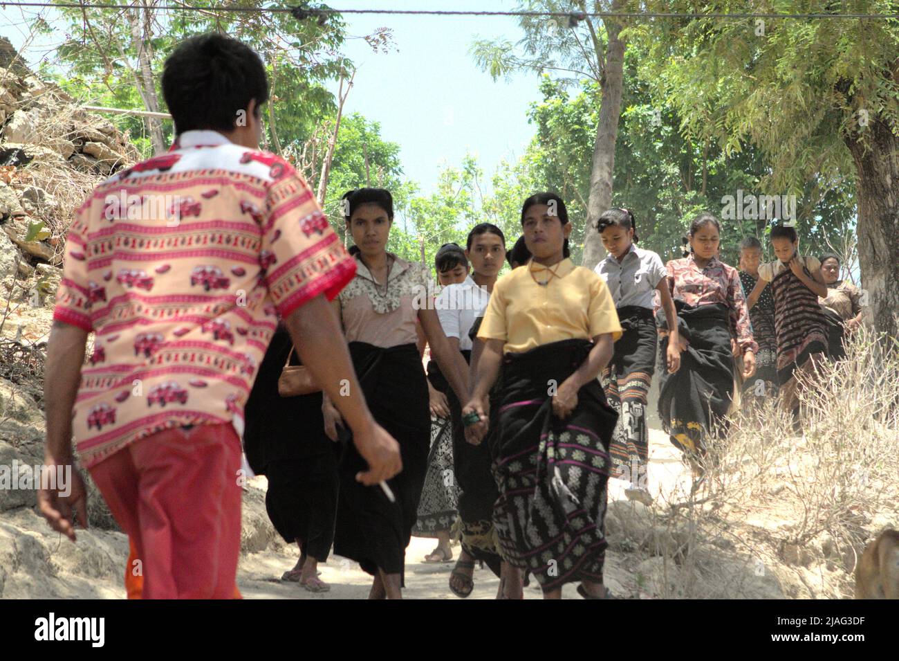 Le donne che camminano su un percorso rurale per partecipare ad una sessione di lutto come un membro della loro comunità è passato via a Kilimbatu, Kawangu, Pandawai, Sumba orientale, Nusa Tenggara orientale, Indonesia. La tradizione legata alla morte nelle comunità Sumbanesi richiede un invito da parte della famiglia in lutto per quanto riguarda chi dovrebbe venire all'evento. Foto Stock