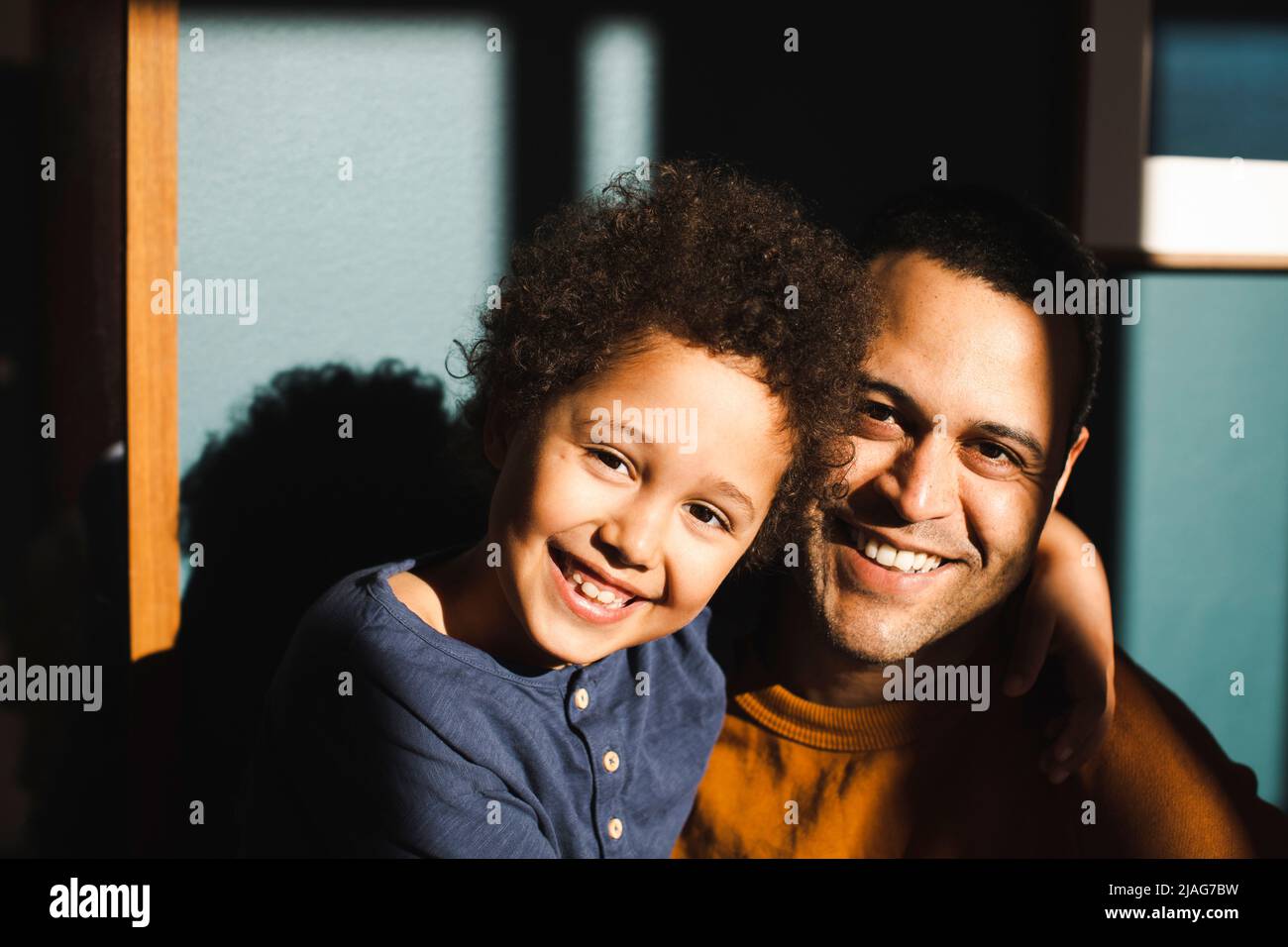 Ritratto di figlio allegro con braccio intorno al padre durante la giornata di sole a casa Foto Stock