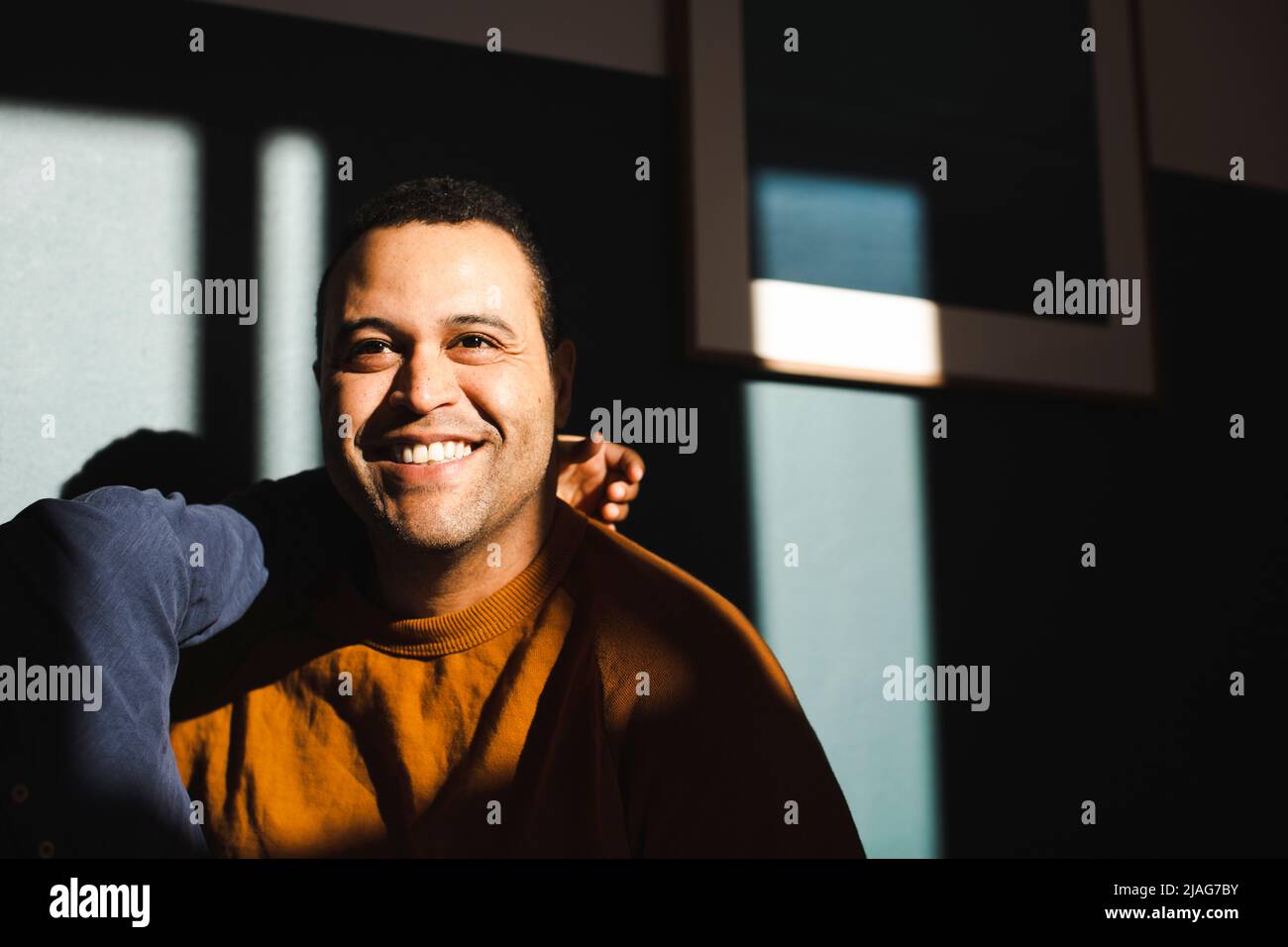 Uomo sorridente con figlio che contempla contro il muro durante la giornata di sole Foto Stock