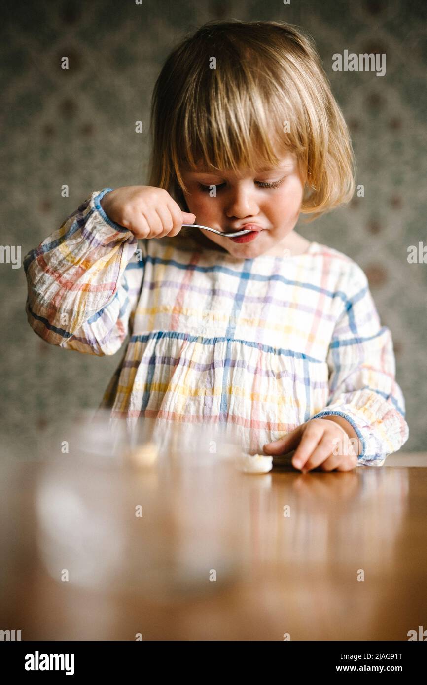 Ragazza bionda con i bangs che mangiano il cibo al tavolo Foto Stock