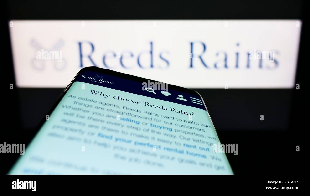 Smartphone con pagina web della società immobiliare britannica Reeds Rains Limited sullo schermo di fronte al logo aziendale. Mettere a fuoco sulla parte superiore sinistra del display del telefono. Foto Stock