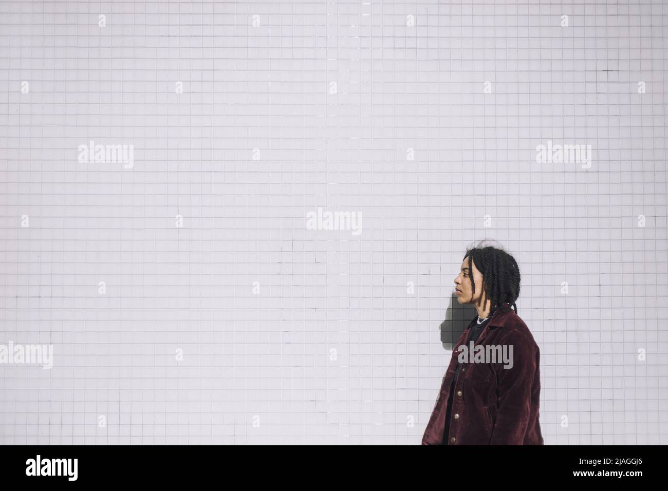 Vista laterale di una persona non binaria in piedi contro il muro durante la giornata di sole Foto Stock