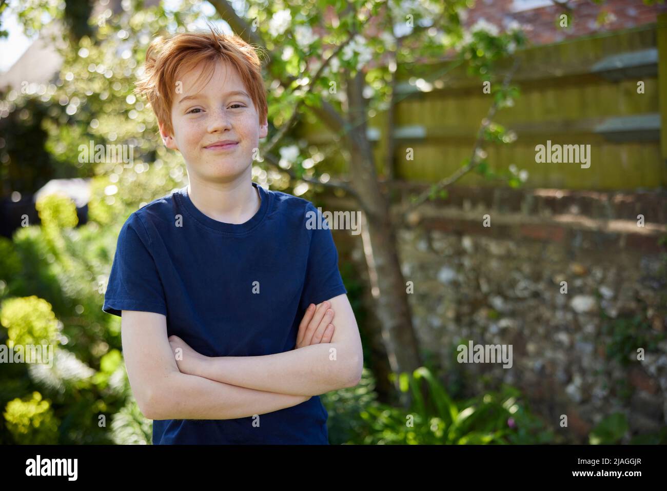 Ritratto di ragazzo sorridente con le braccia incrociate in piedi nel giardino estivo a casa Foto Stock