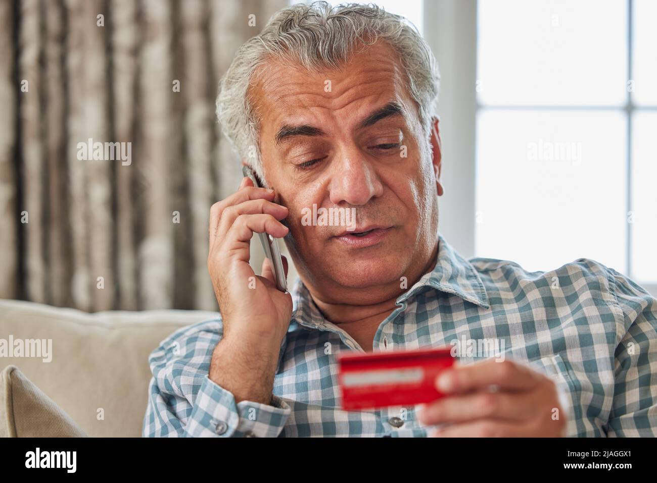 Uomo maturo a casa che fornisce i dettagli della carta di credito sul telefono Foto Stock