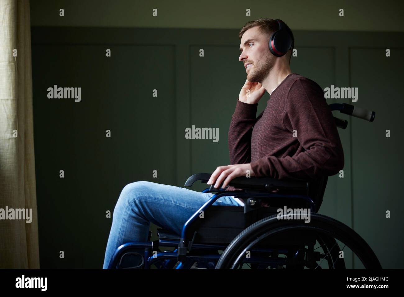 Uomo in sedia a rotelle a casa ascolto di musica o podcast su cuffie wireless Foto Stock