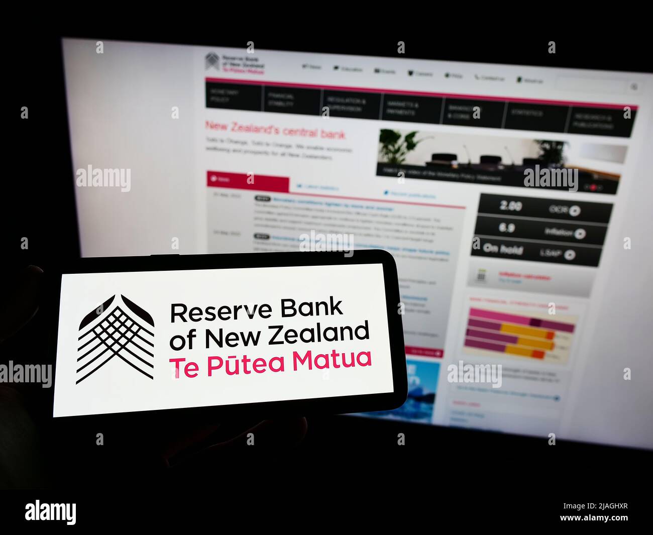 Persona che tiene uno smartphone con il logo della banca centrale Reserve Bank of New Zealand (RBNZ) sullo schermo di fronte al sito web. Mettere a fuoco sul display del telefono. Foto Stock