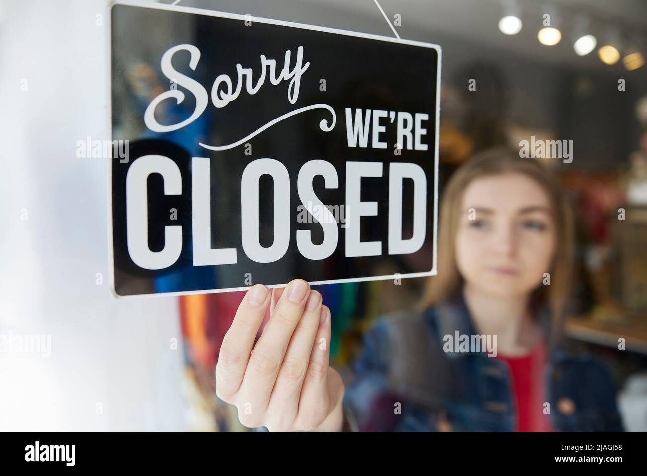 Triste femmina Proprietario di piccola impresa girando rotondo chiuso Sign in Shop Window Foto Stock