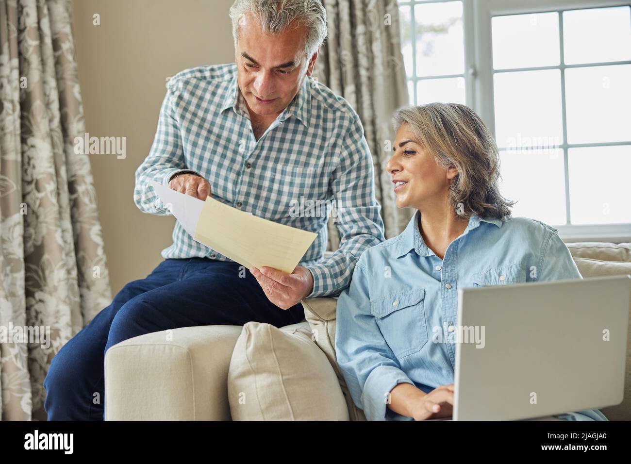Sorridente coppia matura a casa rivedere le finanze nazionali su notebook Foto Stock