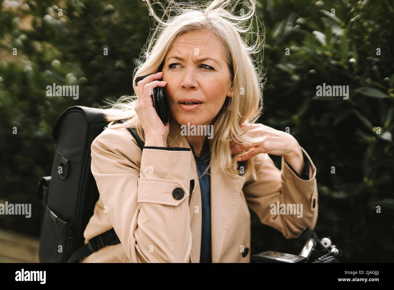 Donna d'affari bionda che contempla mentre parla sullo smartphone Foto Stock