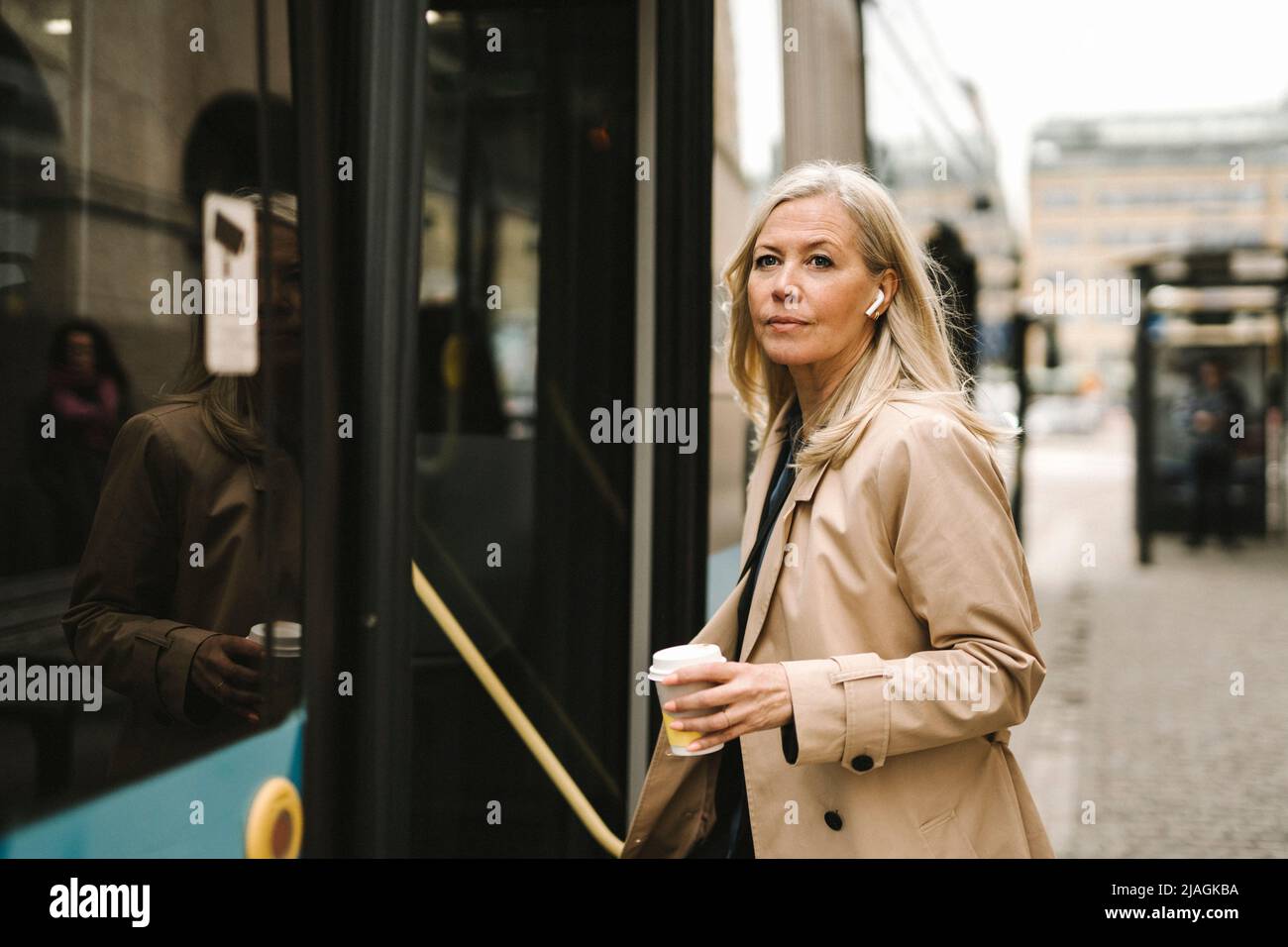 Donna d'affari che tiene una tazza usa e getta mentre si imbarchi sull'autobus in città Foto Stock