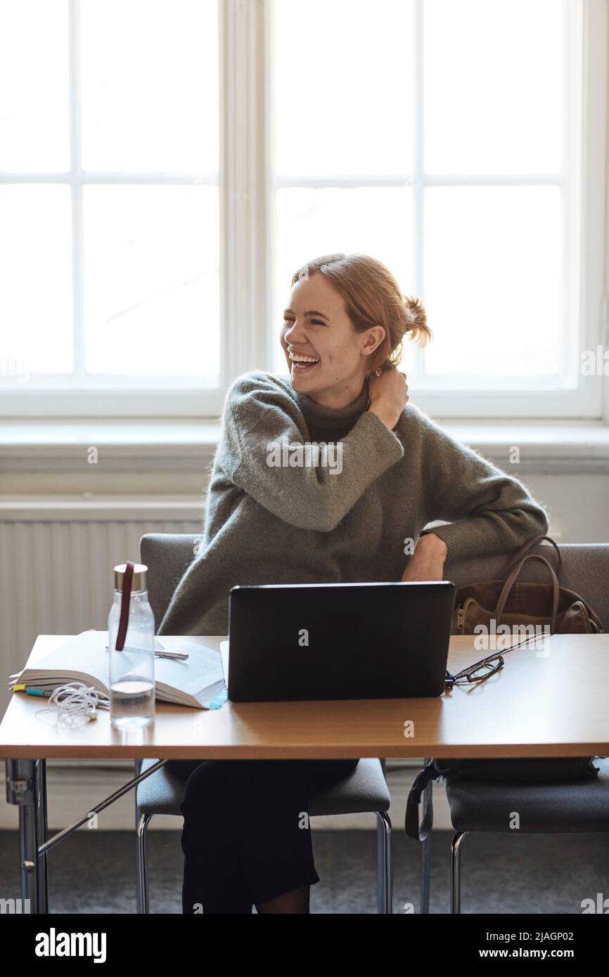 Felice studentessa universitaria seduta con computer portatile sulla scrivania in aula Foto Stock