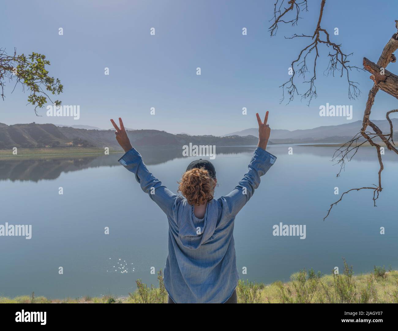 Una donna atletica alza le mani in testa e dà un doppio segno di pace al lago Cachuma, nella contea di Santa Barbara, California. Foto Stock