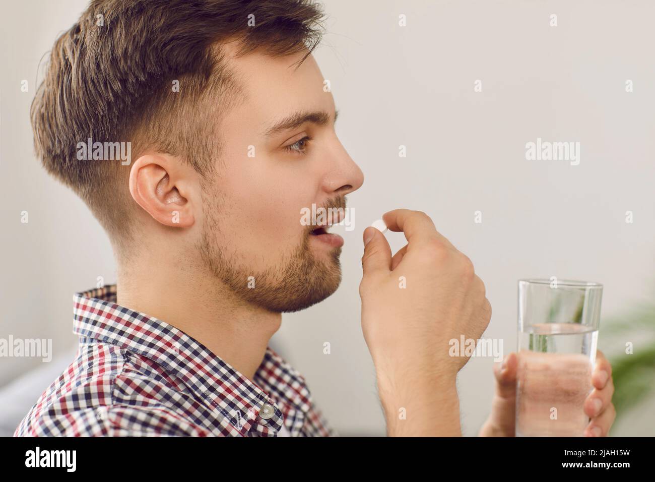 Primo piano di un giovane uomo che assume farmaci prescritti e bere un bicchiere d'acqua Foto Stock
