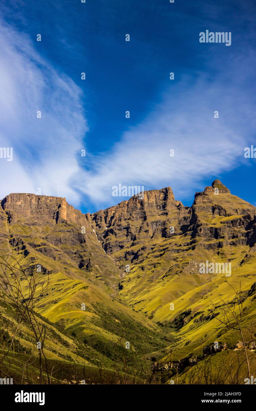 Le alte scogliere scoscese dei Monti Drakensberg, con la neve in bassa stagione ancora leggermente visibile e le nuvole ad alta quota che formano una forma a V. Foto Stock