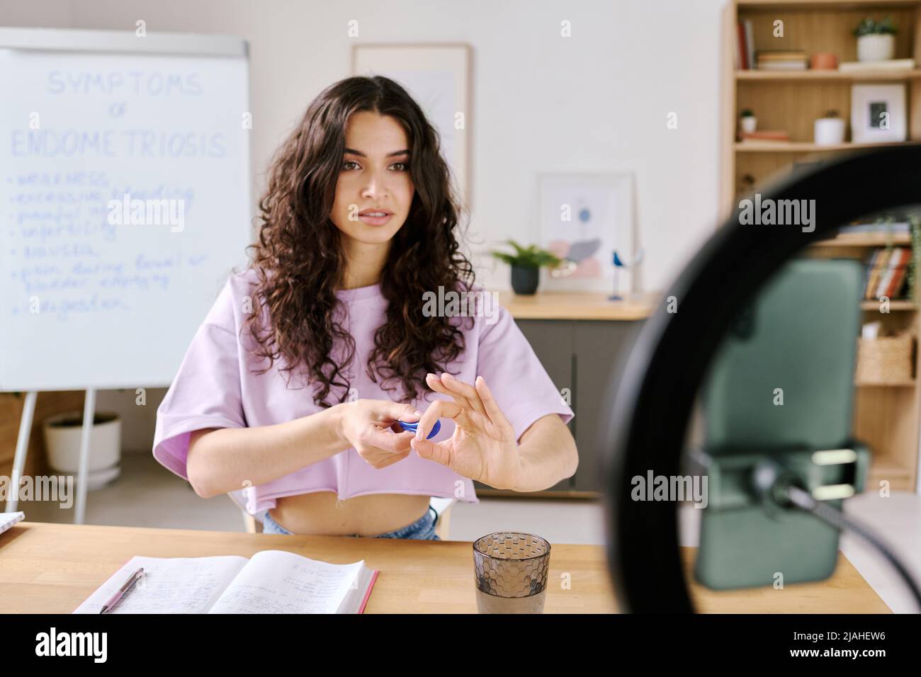 Interessante giovane influencer caucasico seduto di fronte alla fotocamera dello smartphone che spiega come mettere in tazza mestruale Foto Stock