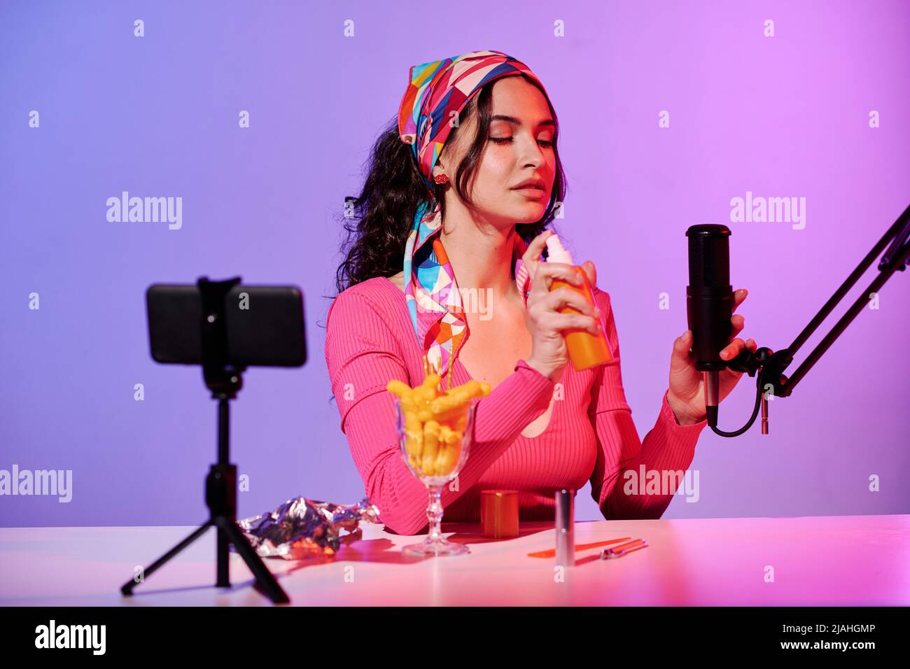 Giovane donna che indossa abiti alla moda seduti in studio registrando il suono ASMR di spruzzare qualcosa Foto Stock