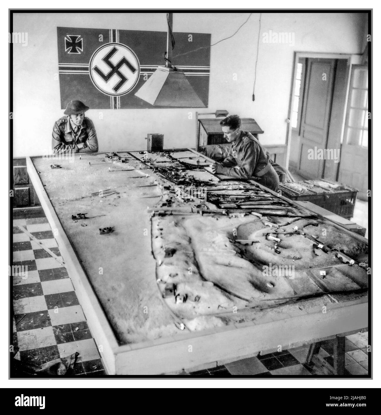 Il D-DAY Juno Beach modello in scala di battaglia nazista di difese realizzate dai pianificatori di battaglia nazisti della costa. Due soldati alleati osservano il modello in scala 3D della difesa nazista in Normandia Juno-Beach nazista a Courseulles sur Mer, in Normandia Francia, con la bandiera tedesca di Swastika alle spalle del 6 giugno 1944 seconda guerra mondiale Foto Stock