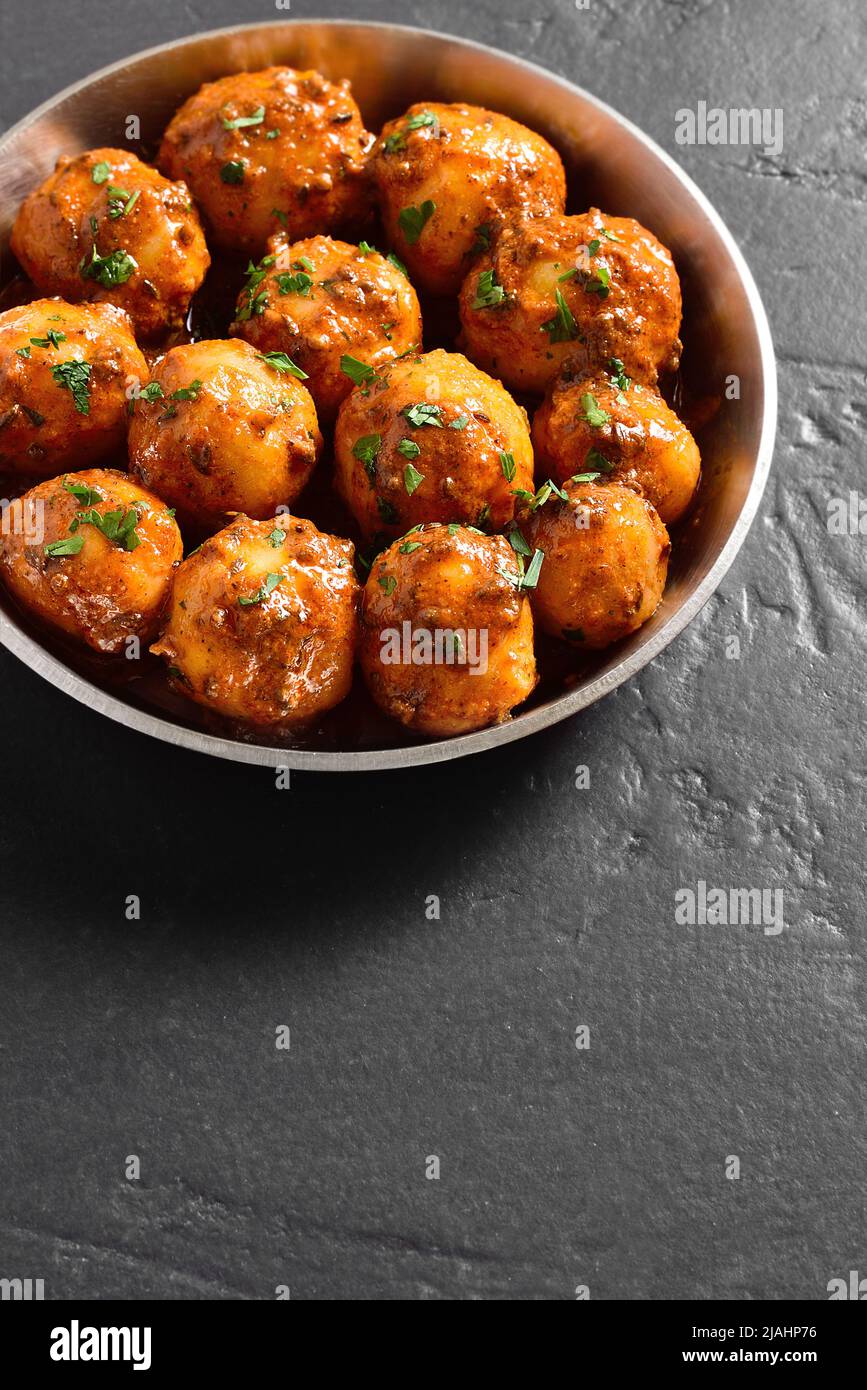 Padella le patate fritte del bambino con i semi di jeera e coriandolo in ciotola sopra il fondo nero della pietra con lo spazio libero del testo. Popolare piatto indiano. Foto Stock