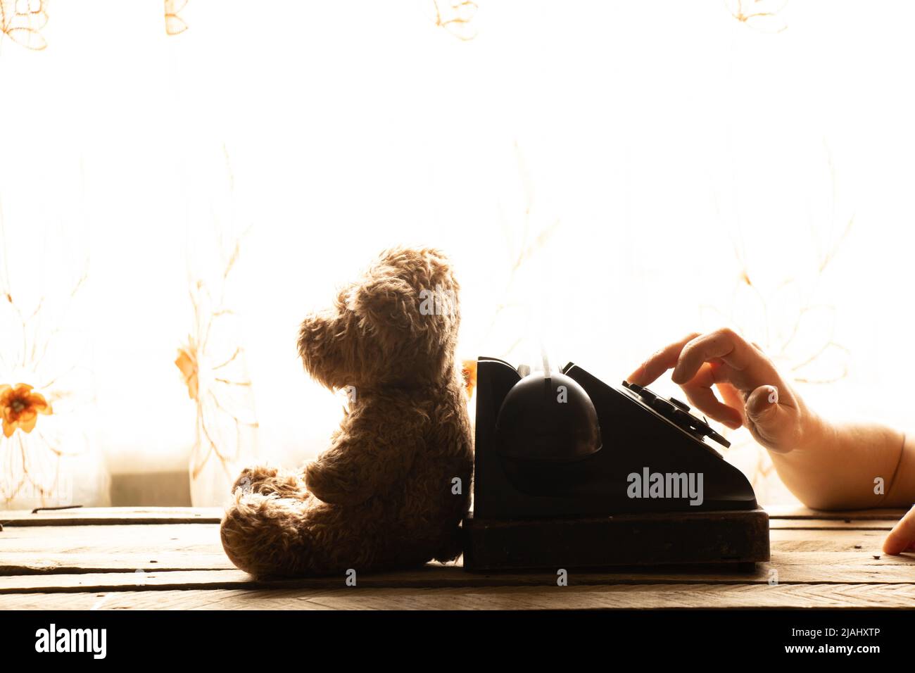 La mano di una donna compone un numero di telefono su un vecchio telefono e un orsacchiotto si siede accanto ad esso a casa sul tavolo, un telefono retrò è nero, una chiamata Foto Stock