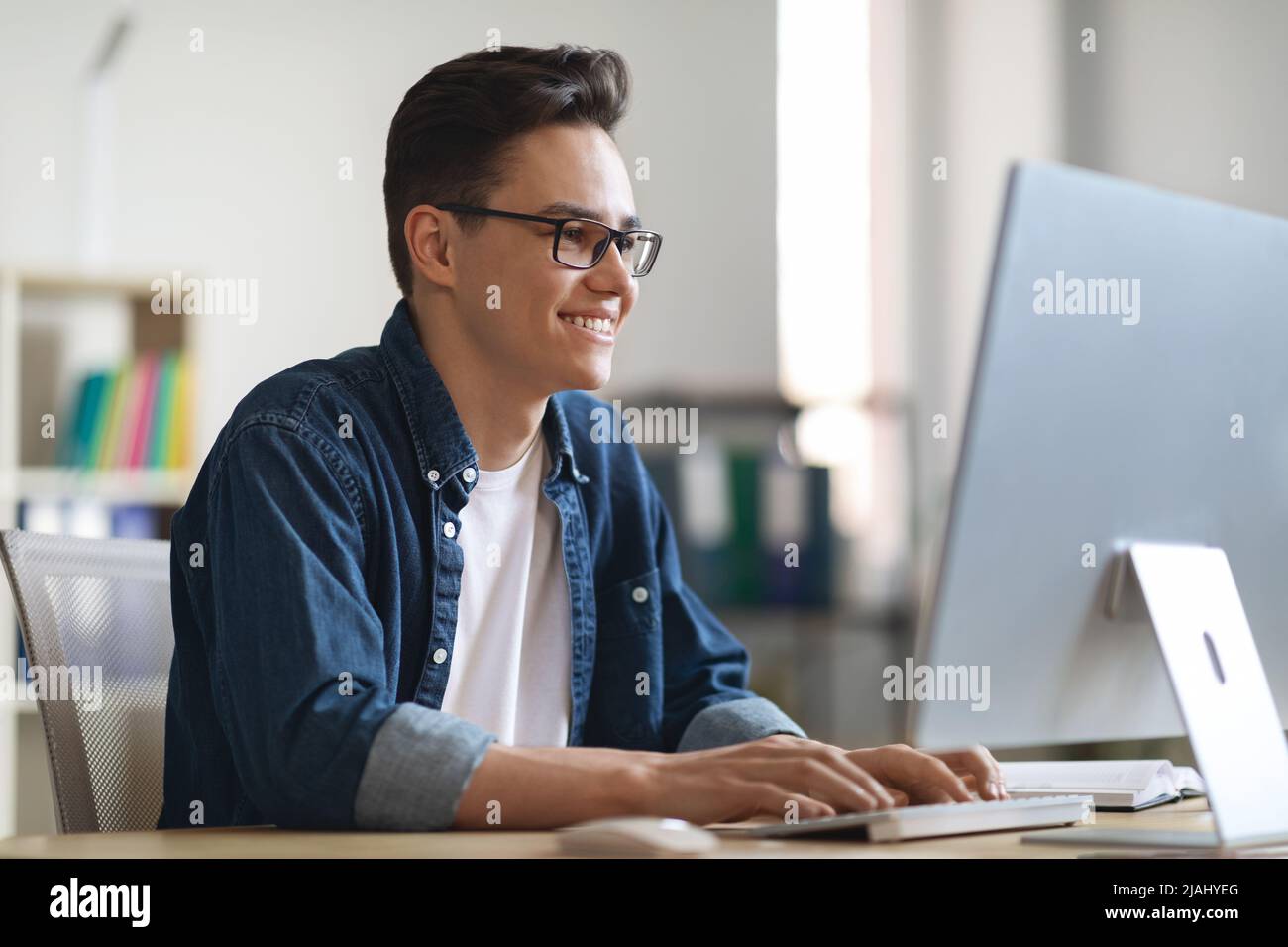 Ritratto di sorridente dipendente di ufficio giovane maschio che lavora su laptop Foto Stock