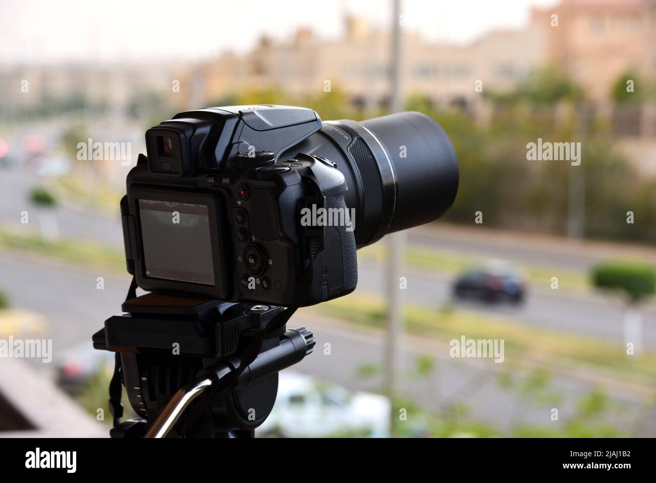 Una fotocamera digitale fissata su un cavalletto per riprese temporizzate e registrazioni video con una vista dall'alto sfocata di una strada cittadina e di edifici, la fotocamera è puntinata Foto Stock