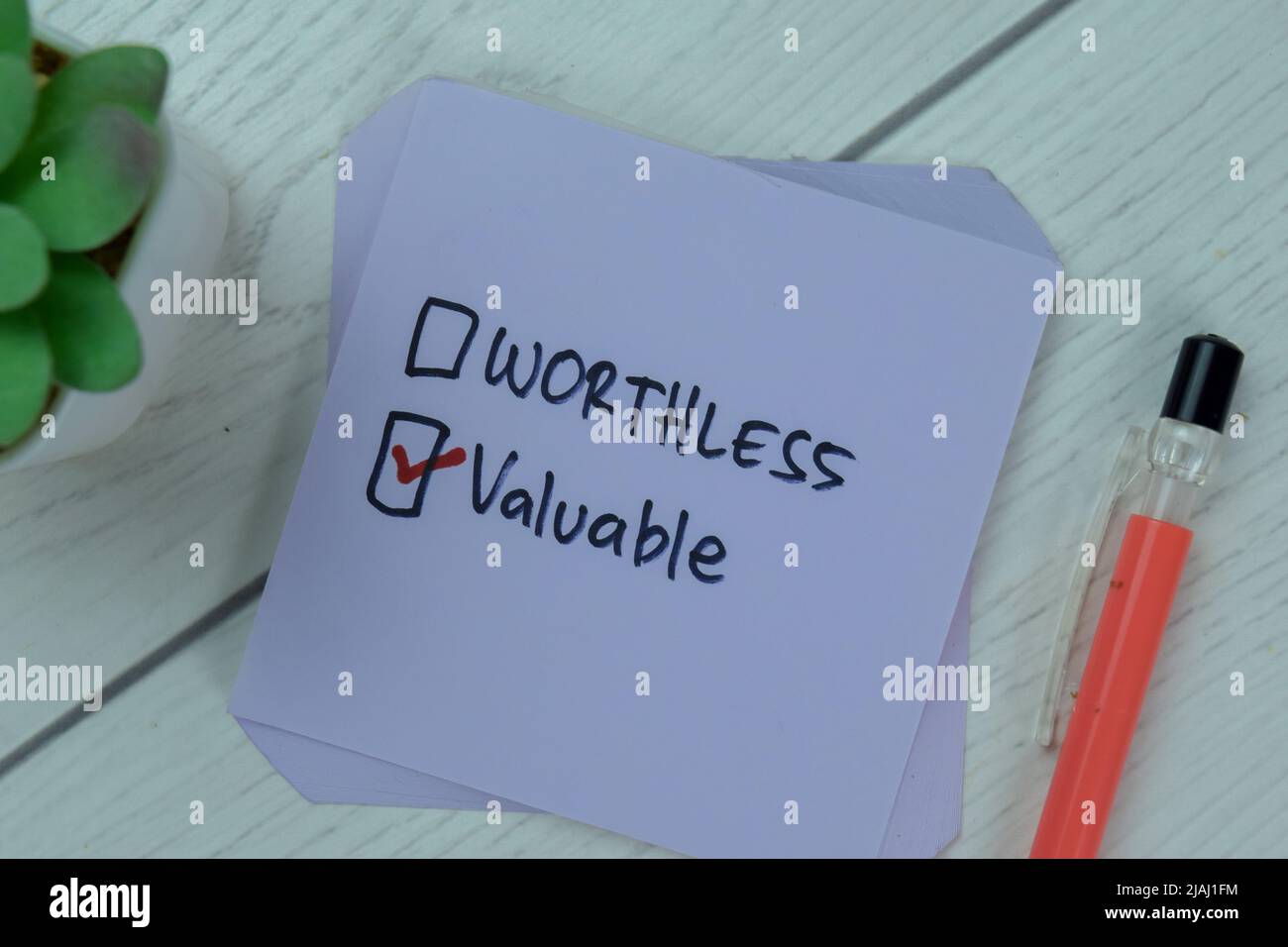 Concetto di inutile o prezioso? Scrittura preziosa su note adesive isolate su tavola di legno. Foto Stock