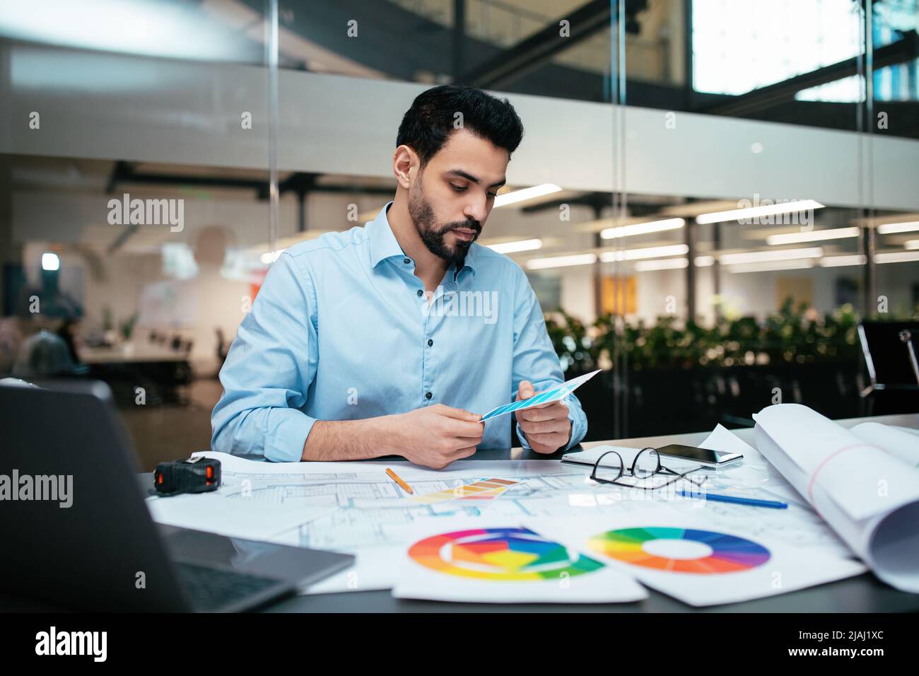 Occupato serio attraente ragazzo designer arabo millennial con barba lavora con tavolozze di colore sul posto di lavoro Foto Stock
