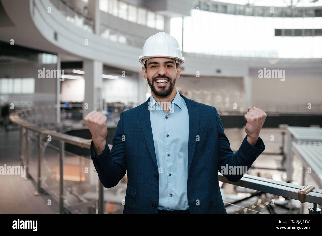 Felice felice emotivo giovane ingegnere arabo maschio costruttore con barba in hardhat rende la mano vittoria gesto Foto Stock