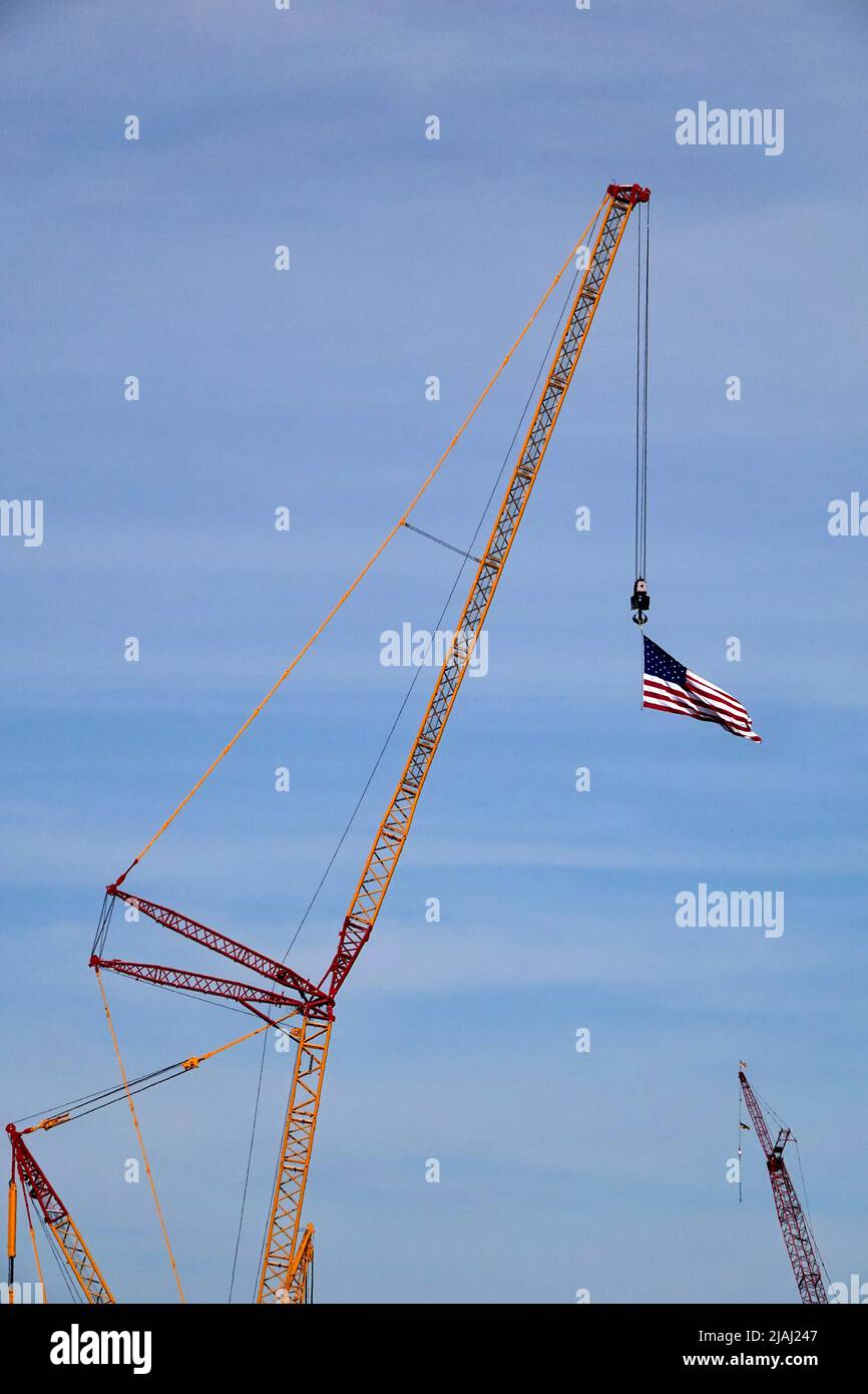 Una bandiera americana soffia nel vento mentre viene trascinata da una gru alta in un cantiere. Foto Stock