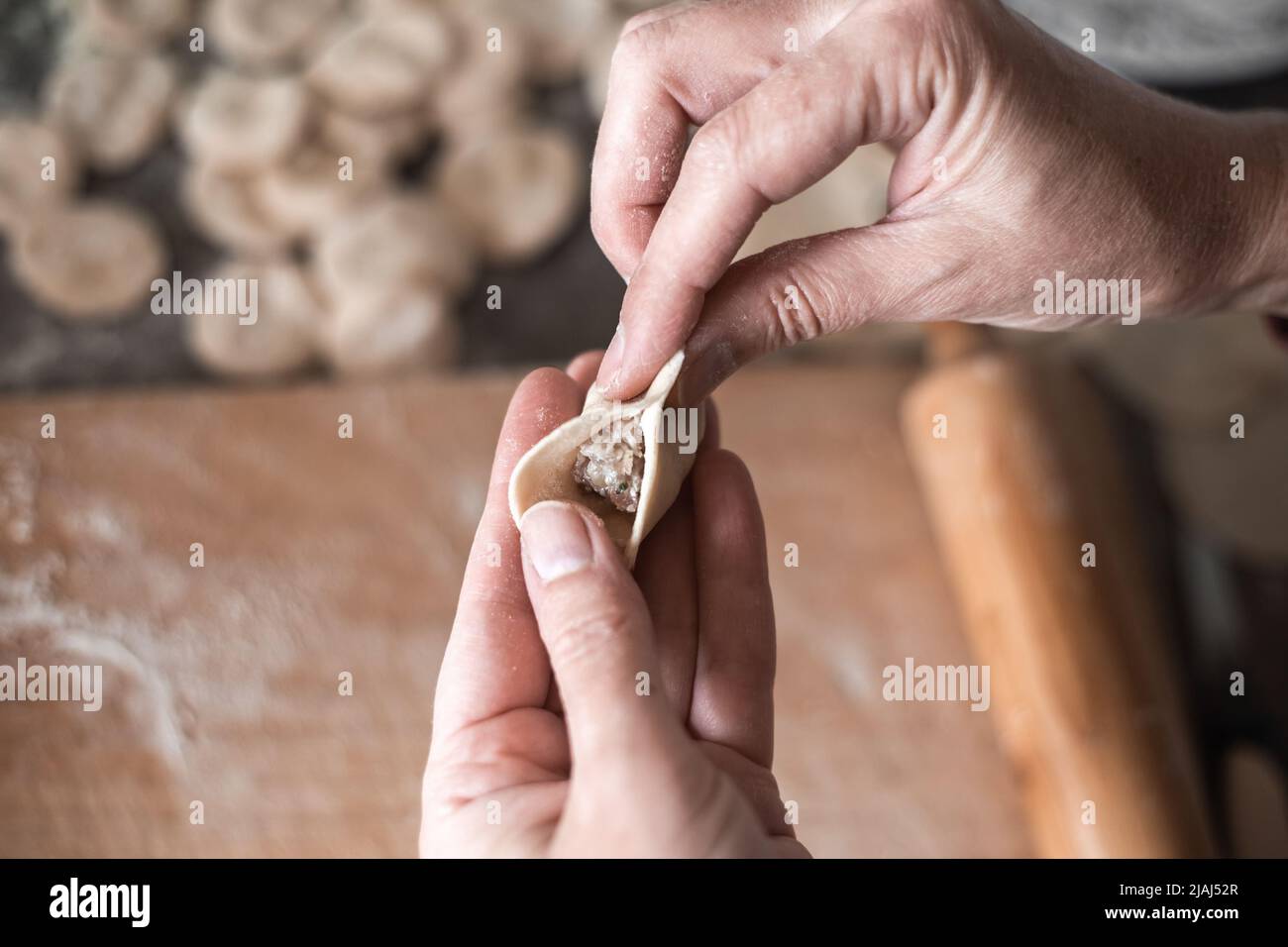 una donna scolpisce gnocchi con ripieno di carne. Cucinare un delizioso piatto russo. Foto Stock